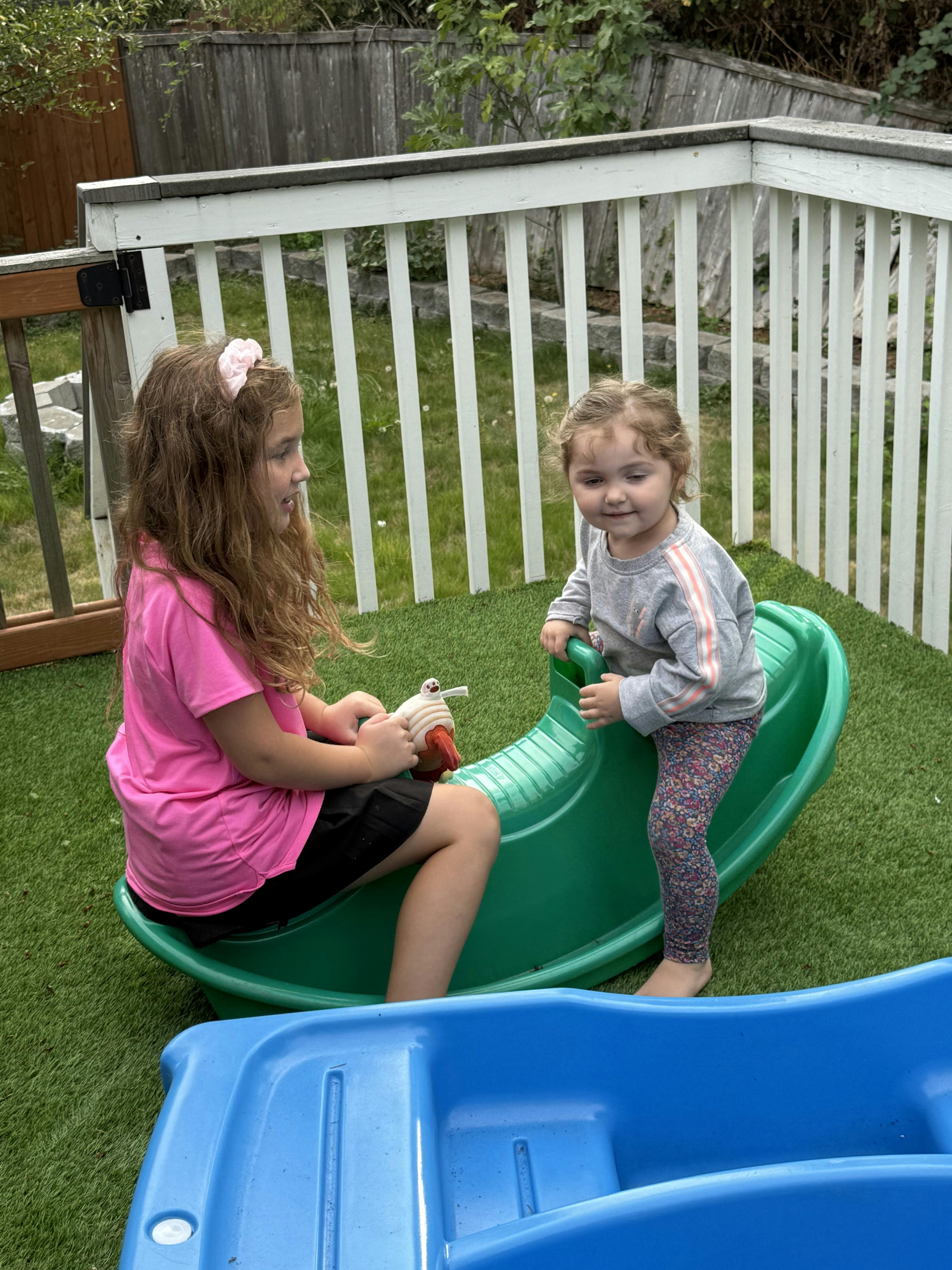 Two children playing on a green plastic seesaw