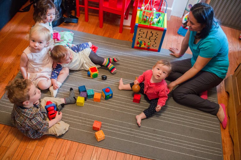 Adult and multiple children playing with blocks on a rug