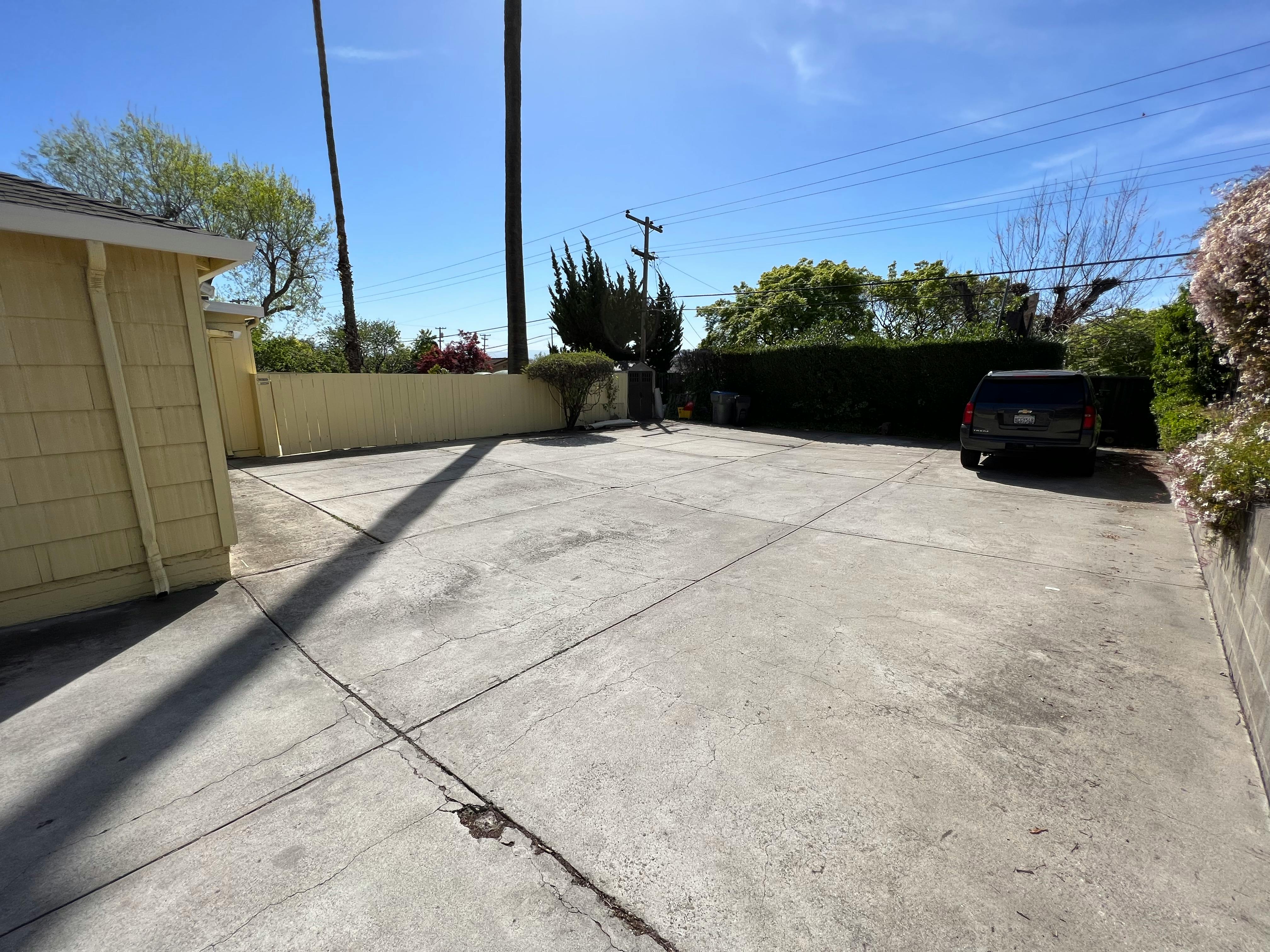 Empty concrete driveway with a building on the left and a vehicle in the background