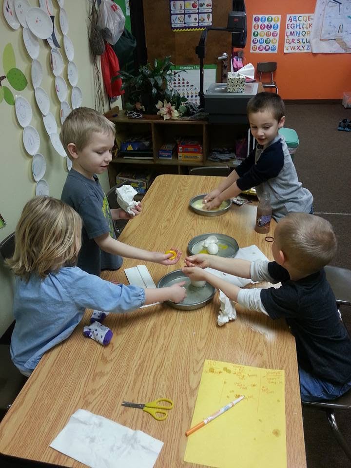 Four children at a table playing with bowls of water and small objects