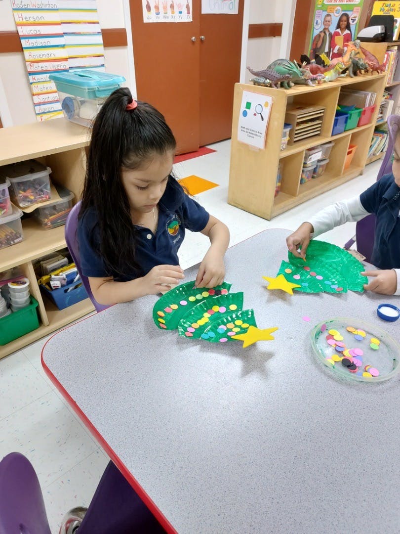 Child decorating a paper Christmas tree with colorful stickers in a classroom