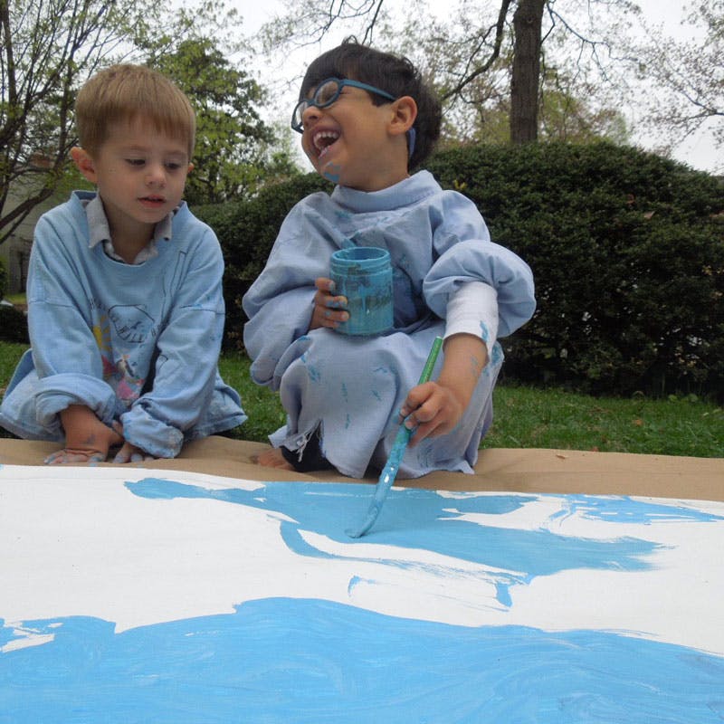Two children painting on a large white surface outdoors