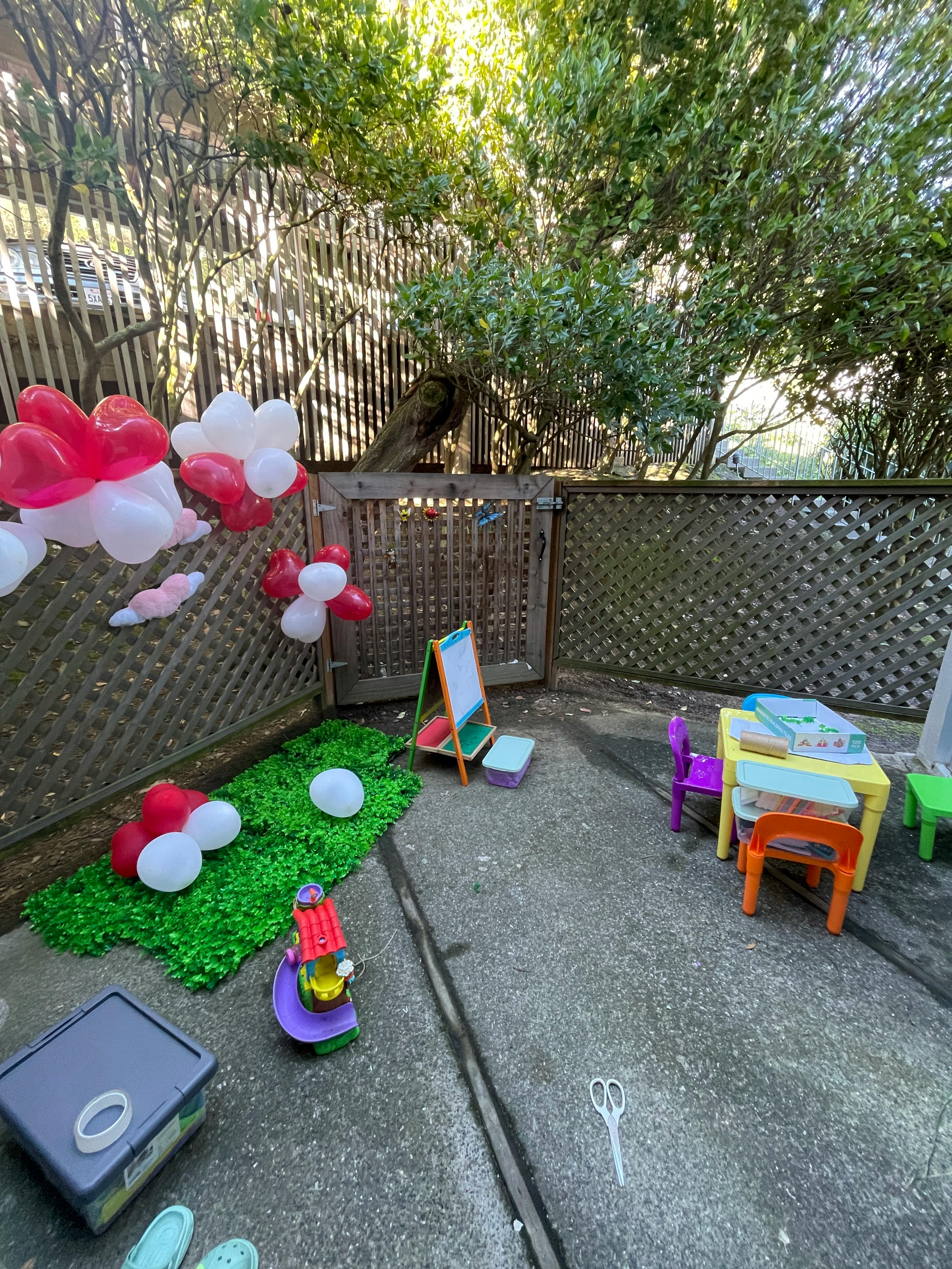 Outdoor play area with balloons, small table and chairs, and an easel
