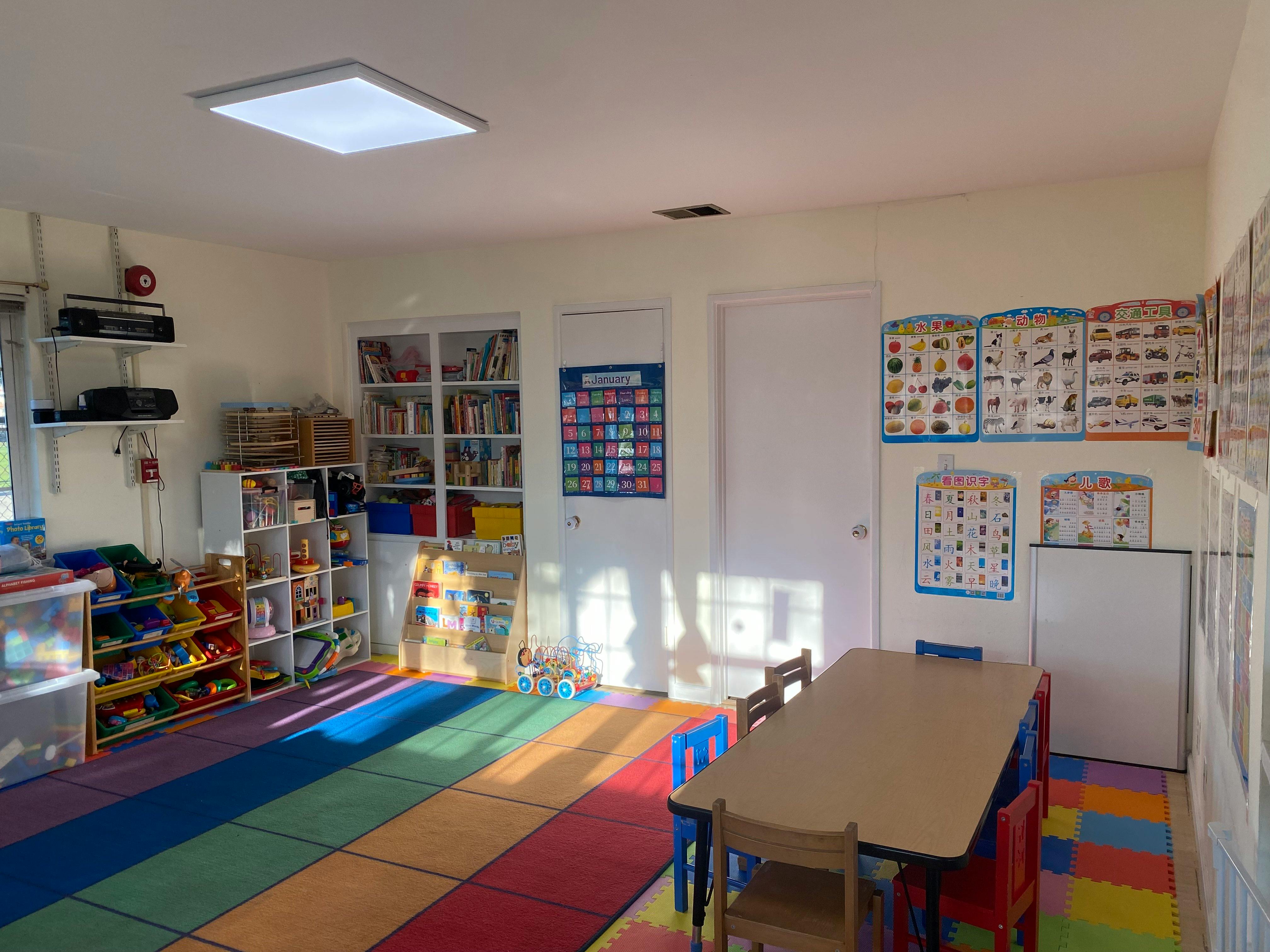 Classroom with colorful rug, small tables and chairs, and shelves with books and toys