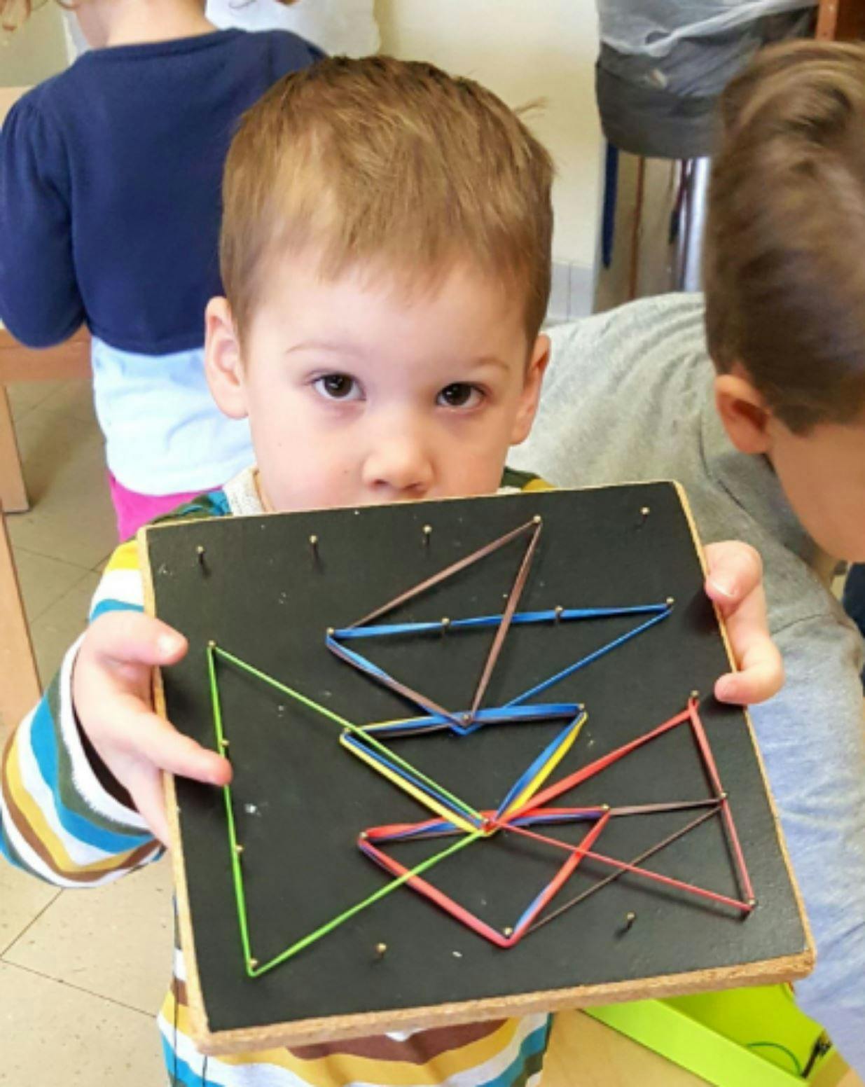 Child holding a geoboard with colorful rubber bands forming shapes