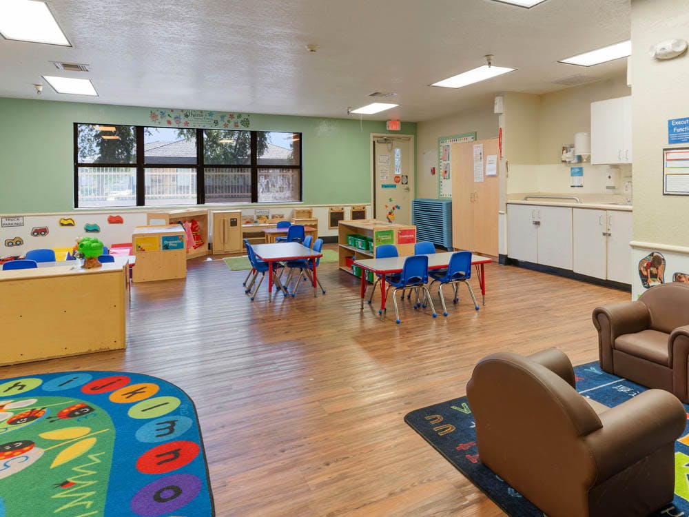 Empty children's classroom with small tables, chairs, and play areas