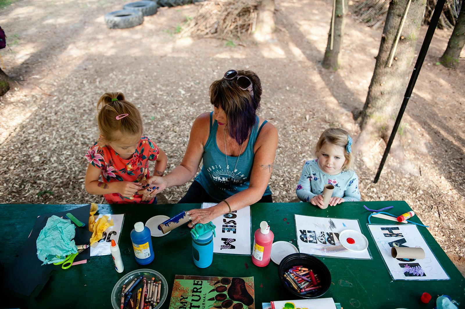 Person and two children painting at a table outdoors