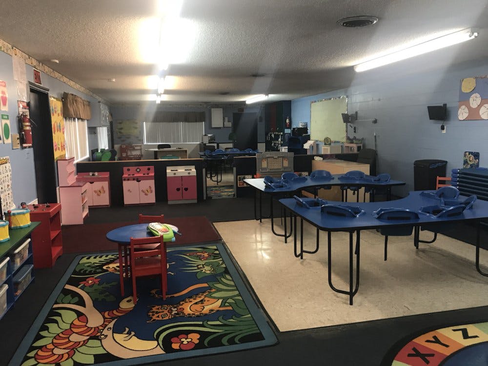 Classroom with small blue tables and chairs, colorful rug, and pink storage units