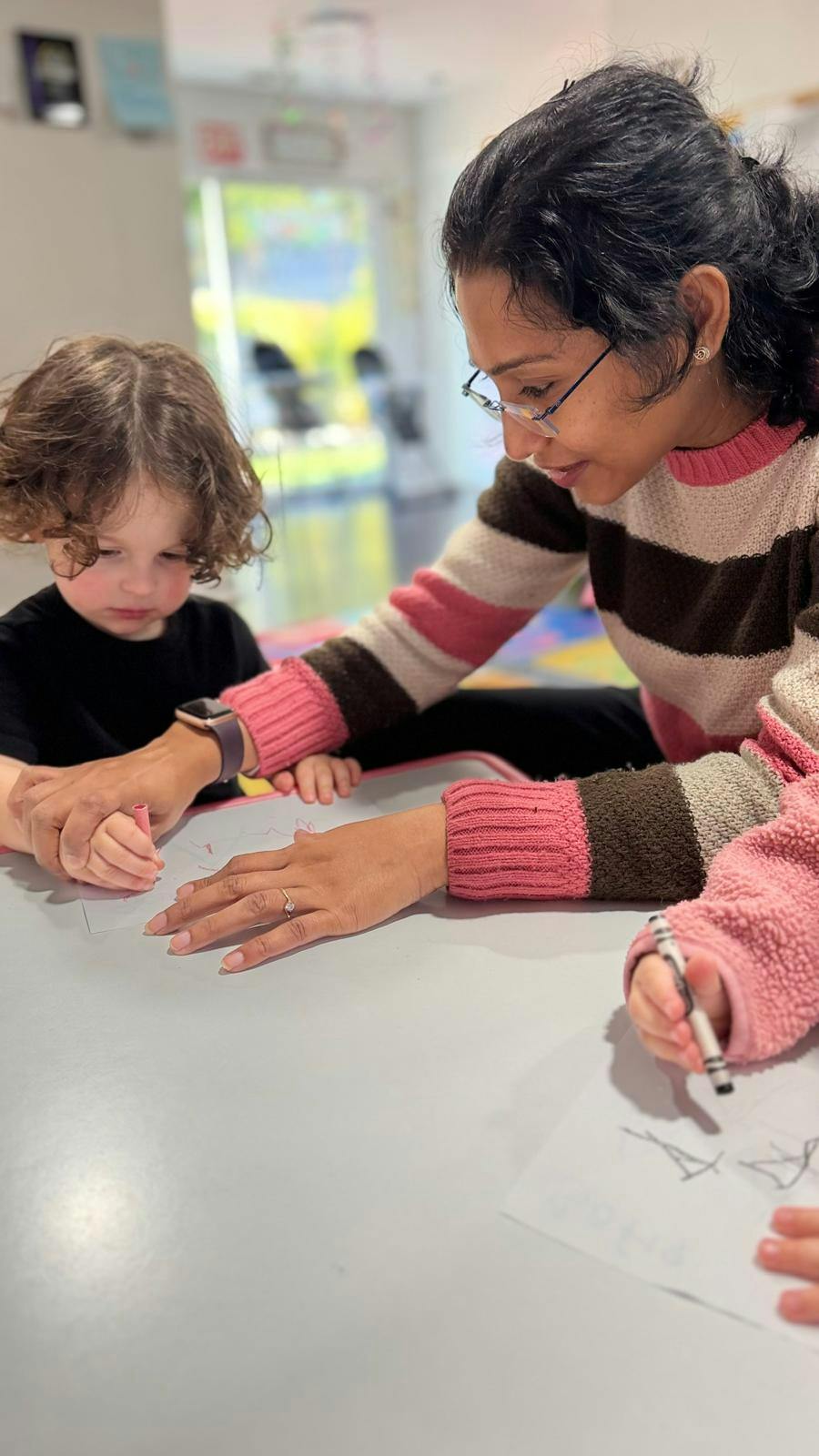 Adult assisting a child with drawing at a table