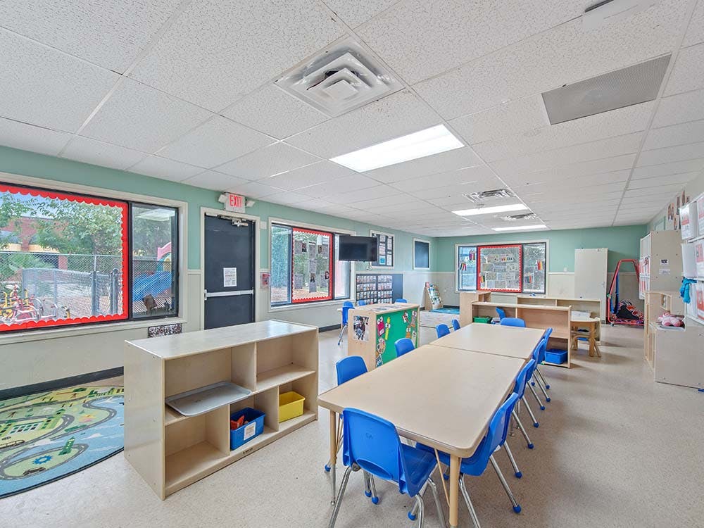 Classroom with tables, blue chairs, shelves, and large windows