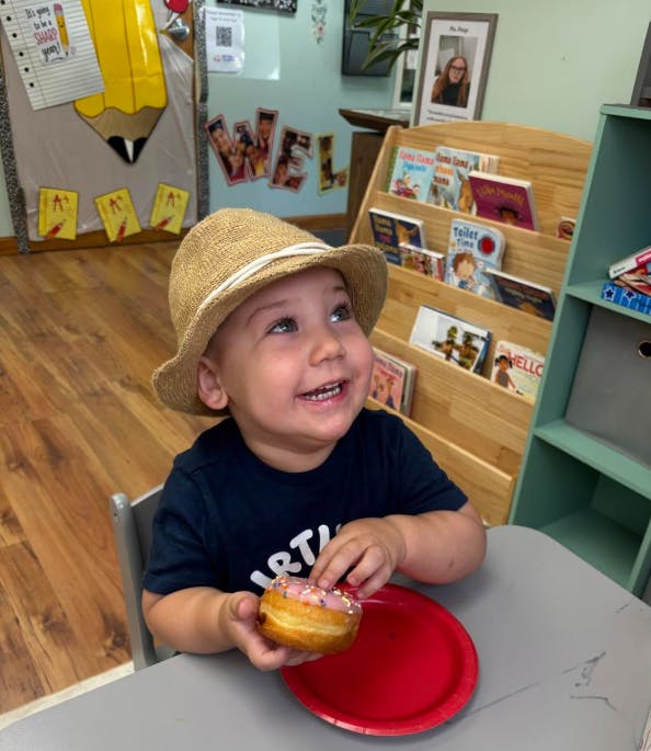 Child wearing a bucket hat holding a donut in a classroom