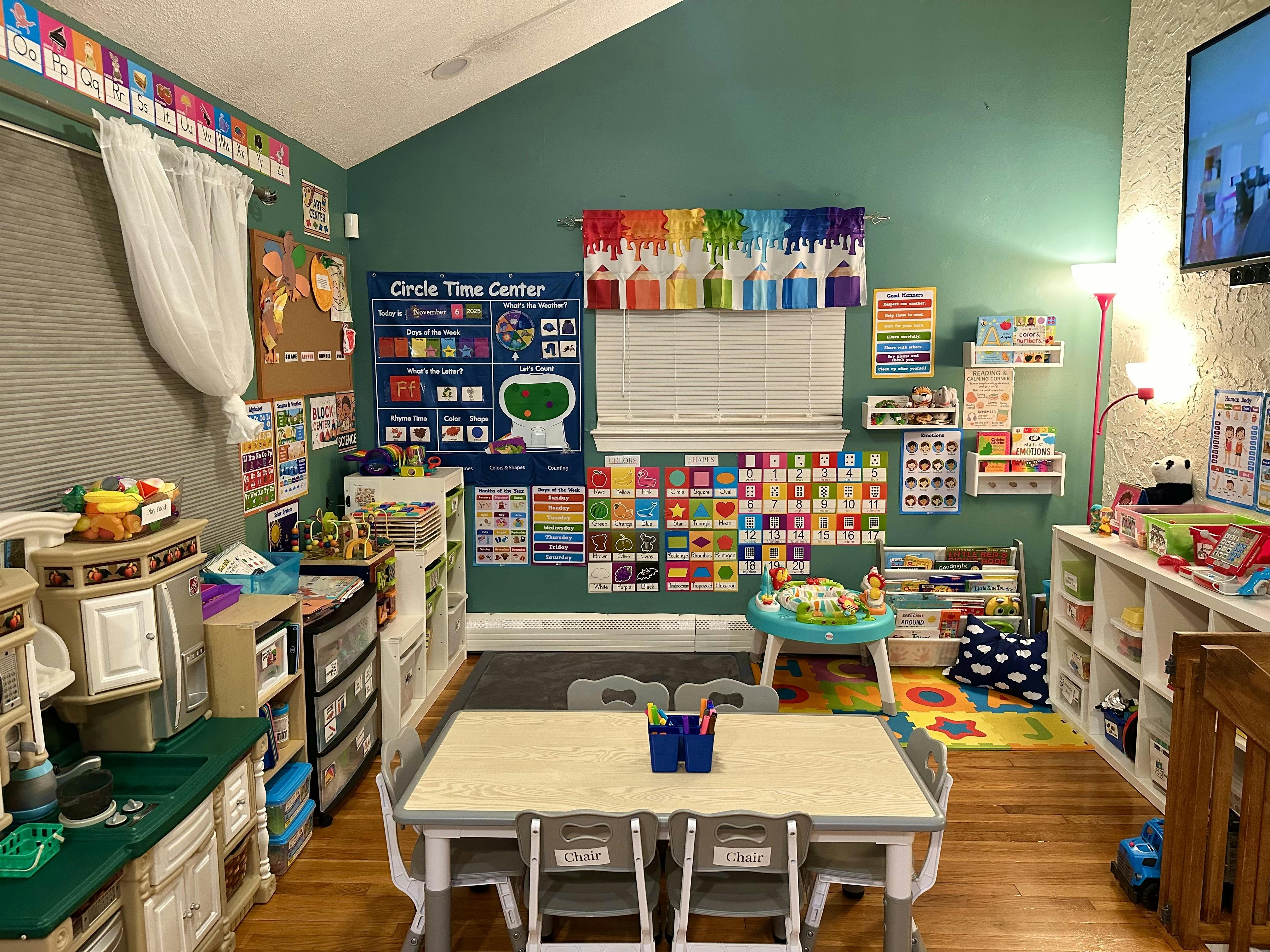 A colorful classroom with a table and chairs, play kitchen, and learning charts