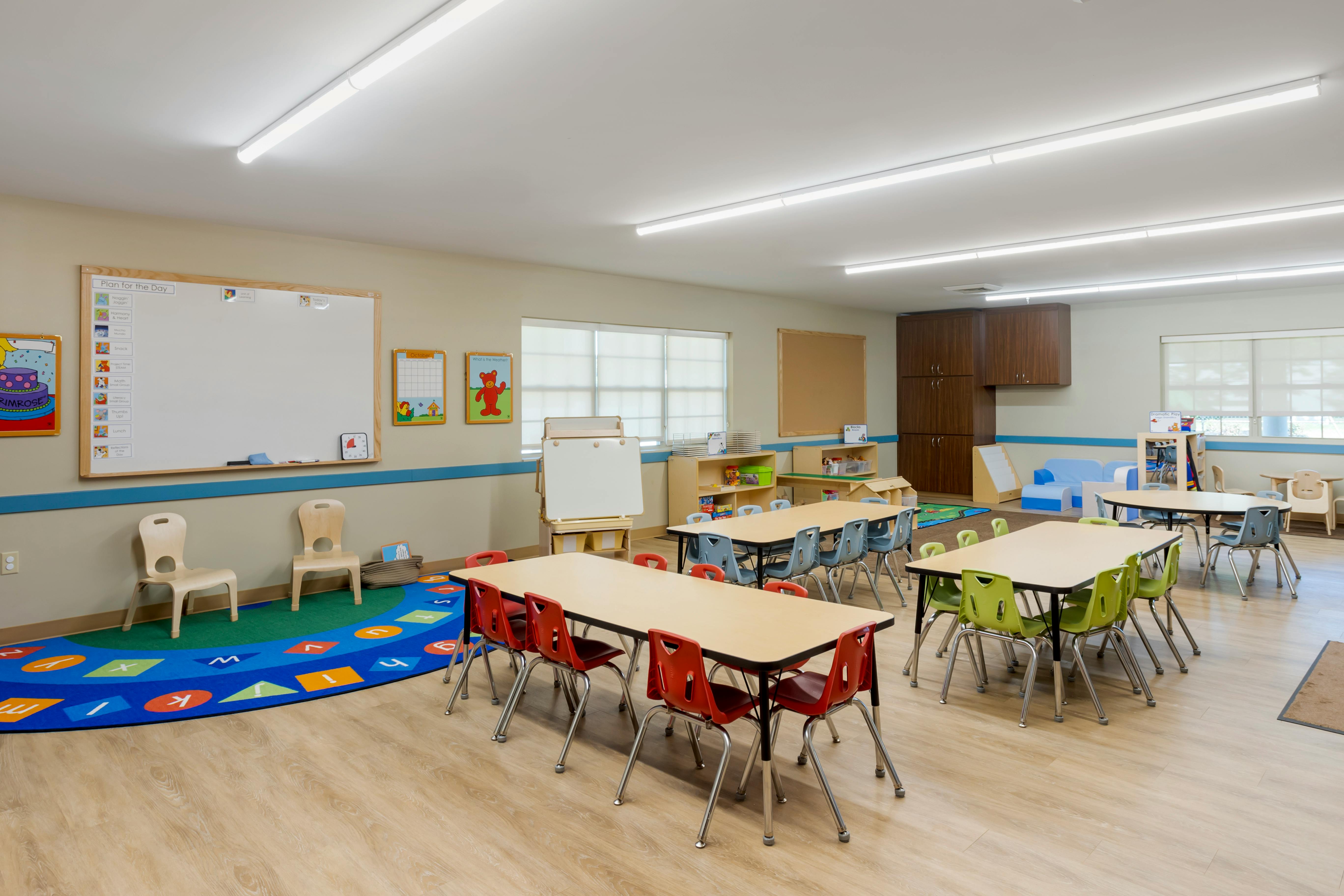 Classroom with multiple tables and chairs, whiteboards, and play areas