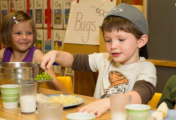 Child serving peas from a bowl, another child smiling nearby