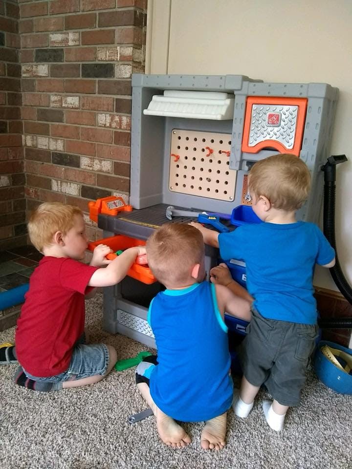 Three children playing with a toy workbench