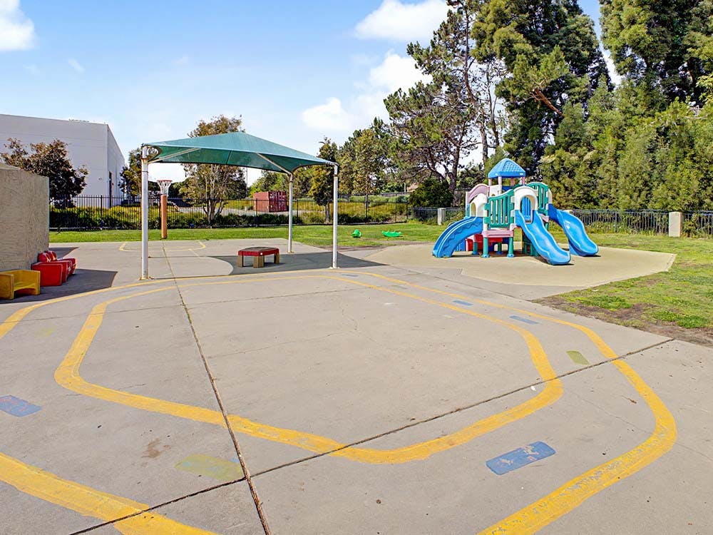 Outdoor playground with a climbing structure, slides, and shaded area