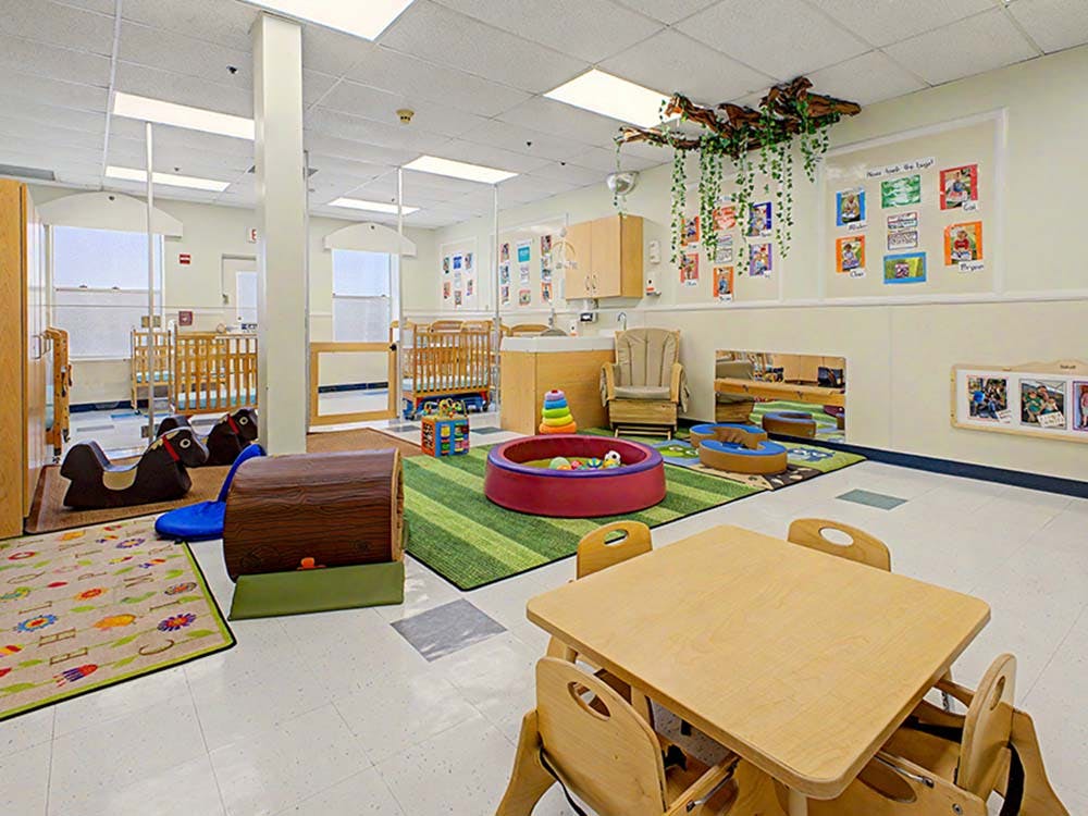 A colorful childcare classroom with cribs, play mats, and a small table with chairs