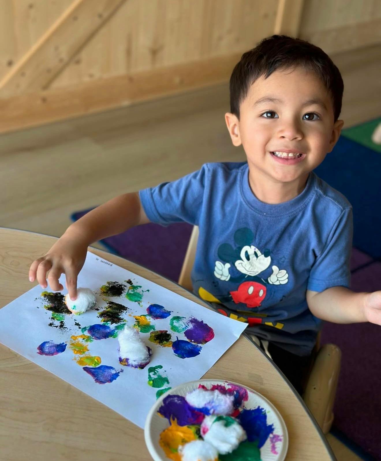 Child smiling while sponge painting in a classroom