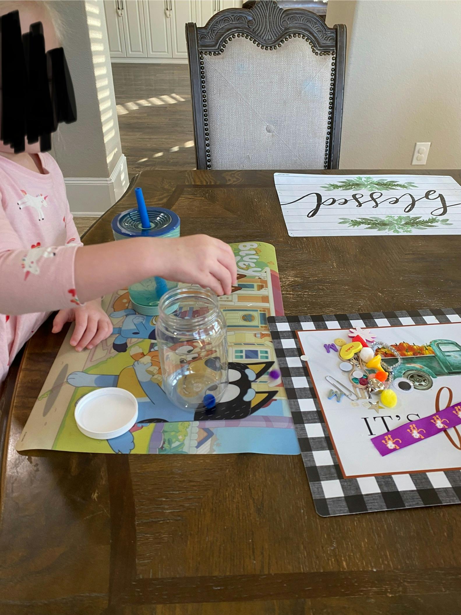 Child's hand placing an object into a glass jar on a table