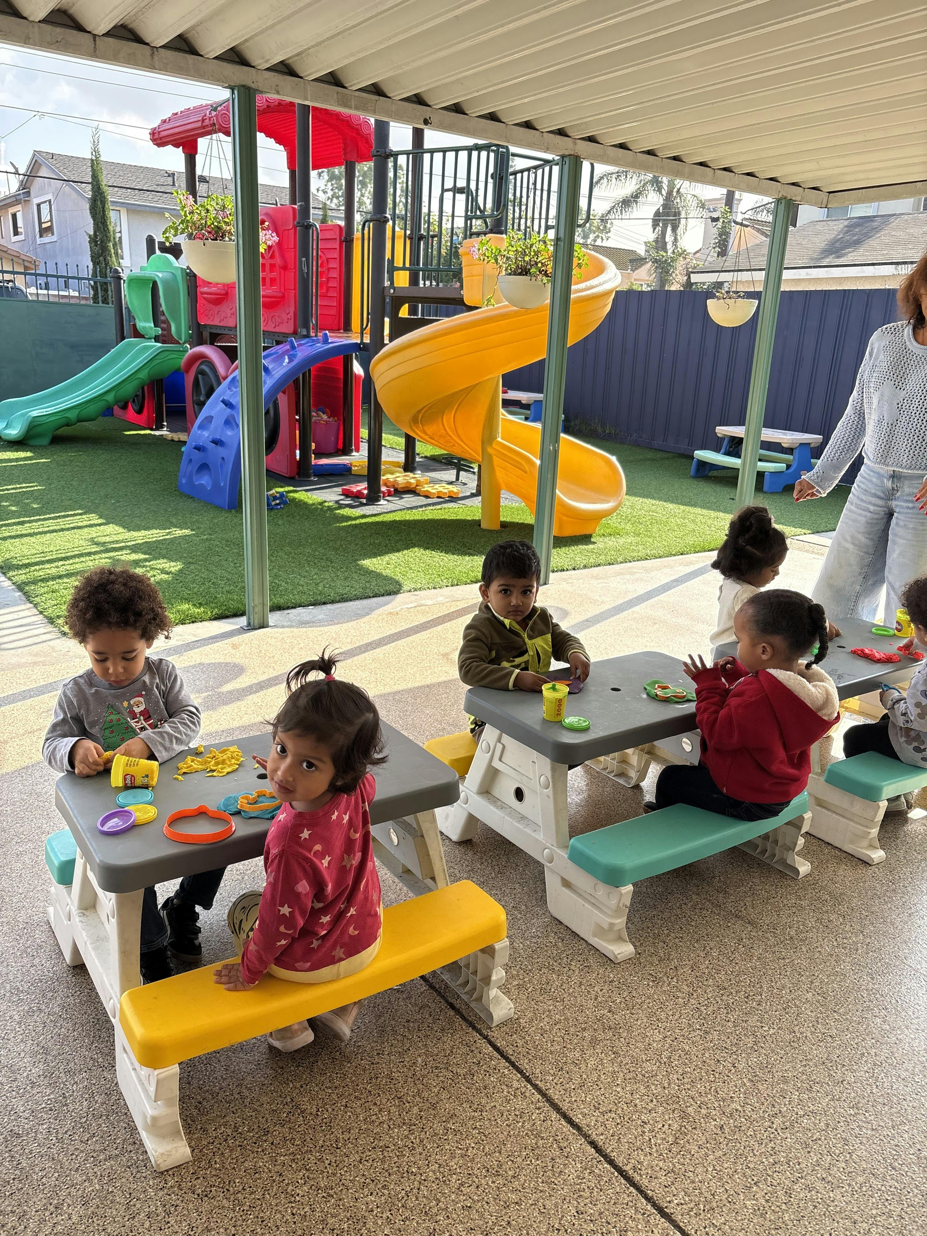 Children playing with clay at small picnic tables on a patio