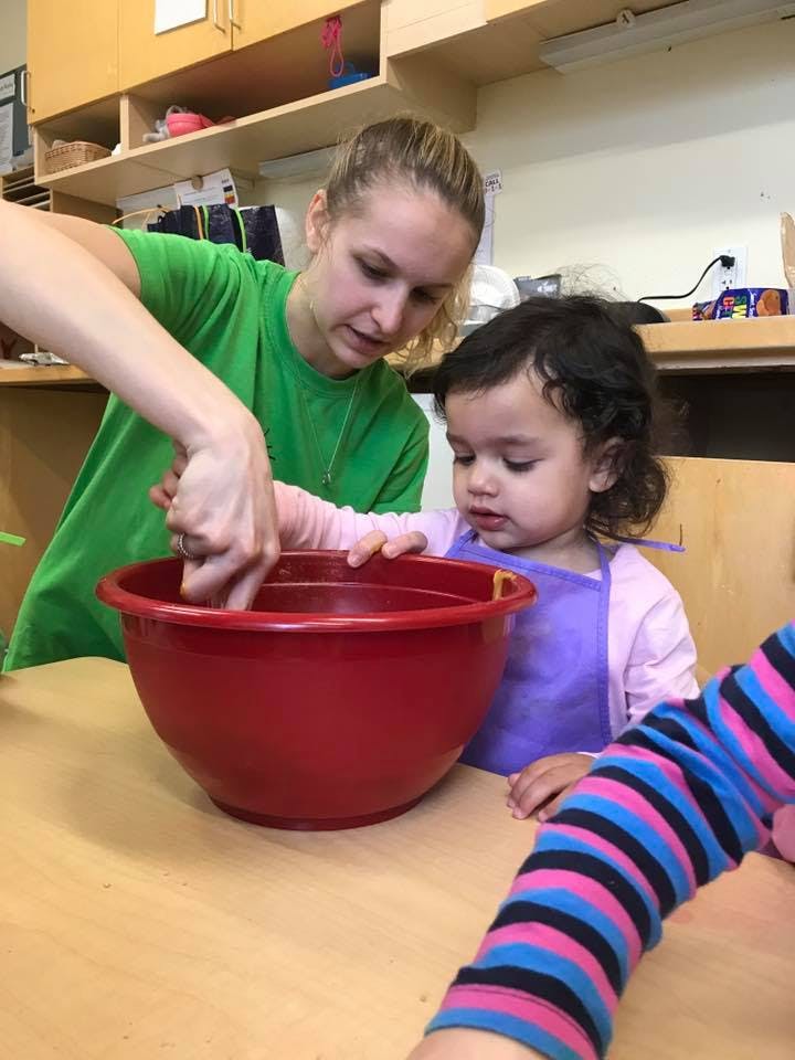 Person helping a child mix ingredients in a red bowl