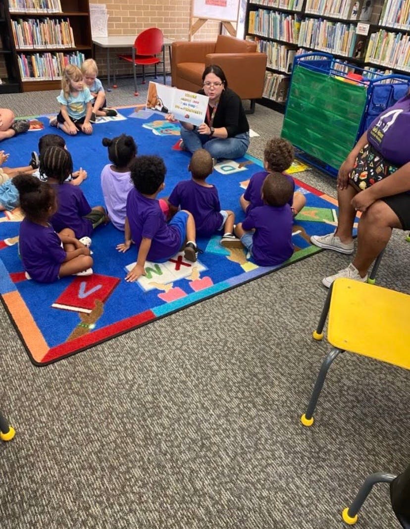 Adult reading a book to a group of children sitting on a library rug