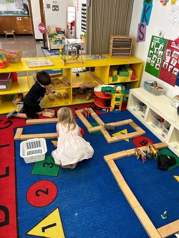 Two children playing with wooden blocks on a blue rug in a classroom