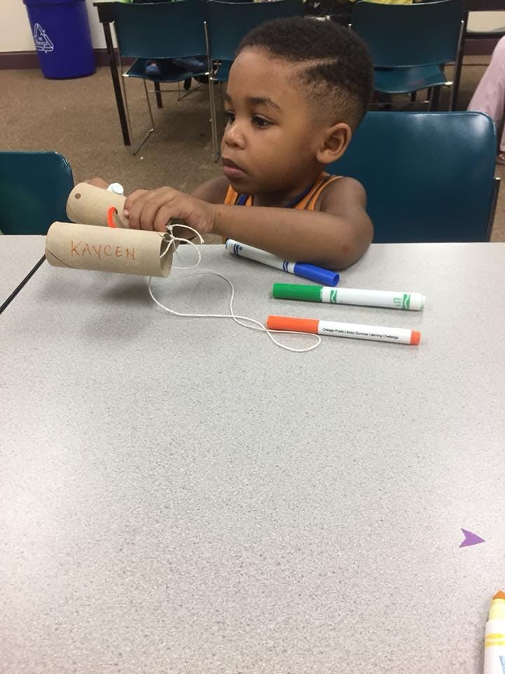 Child at a table holding two cardboard tubes connected by string