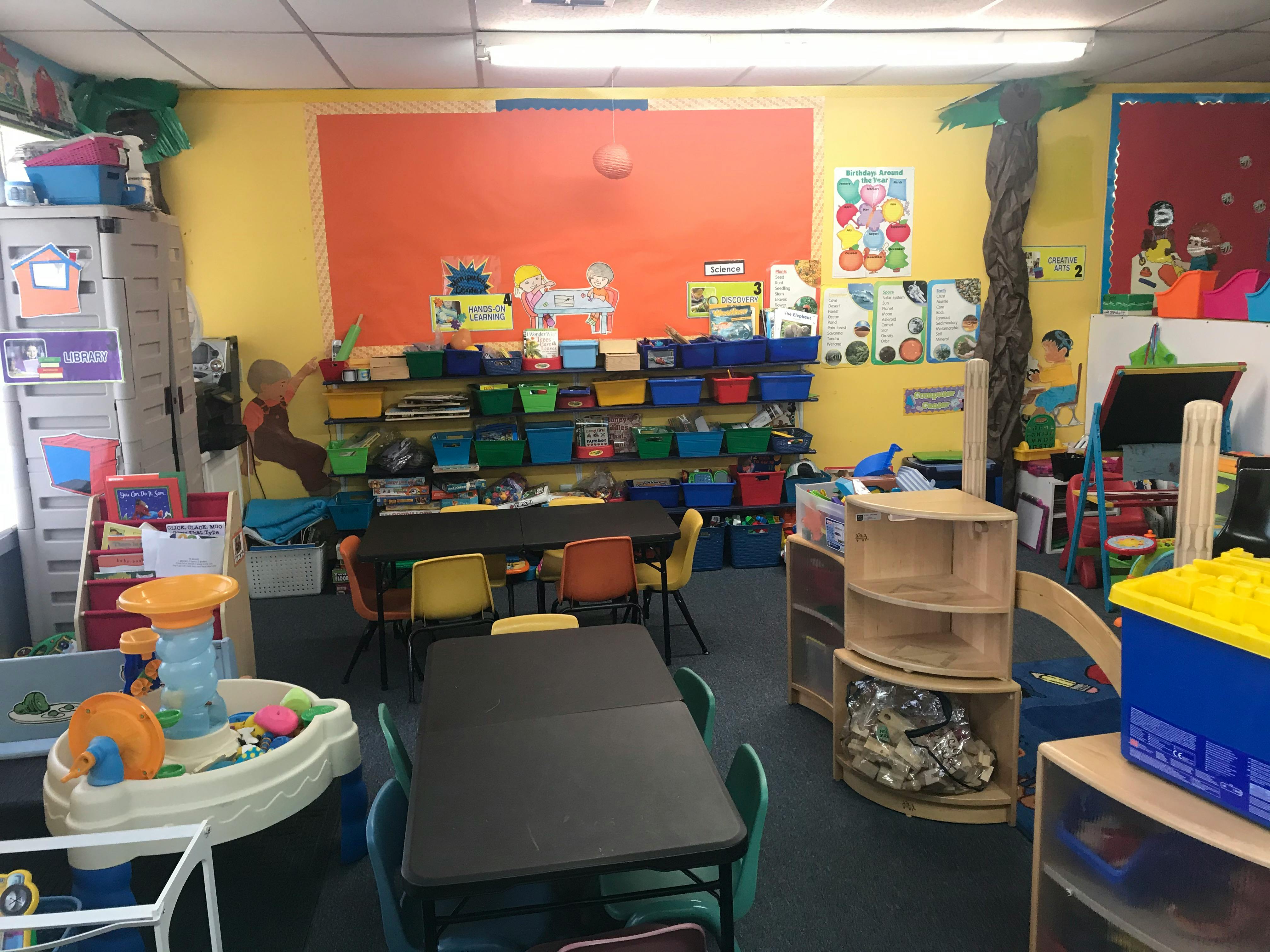 Classroom with tables, chairs, shelves with bins, and colorful decorations