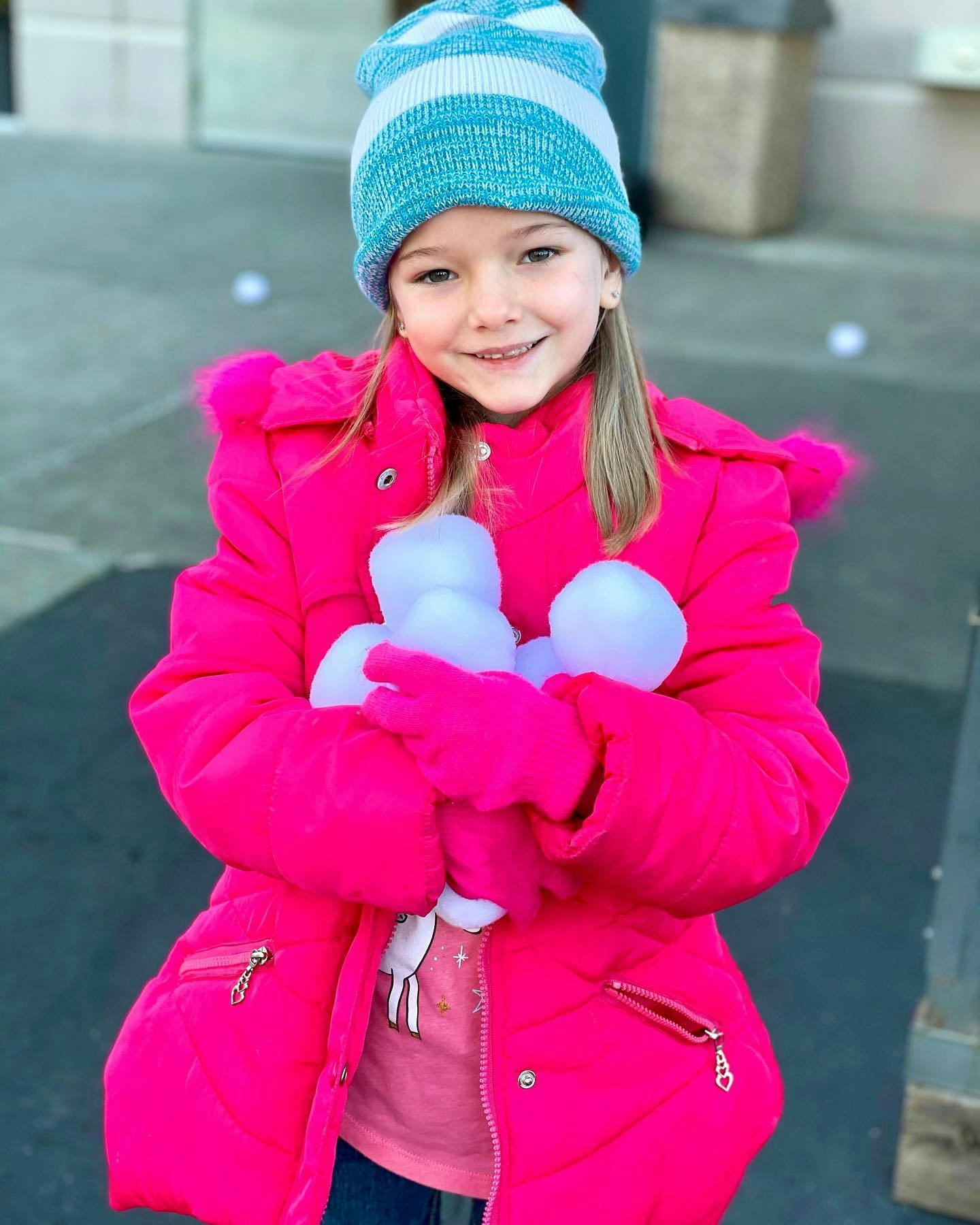 Child in winter coat and hat holding white objects