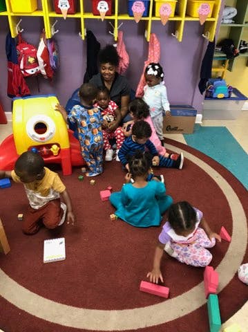 Adult and multiple children playing with toys on a red rug