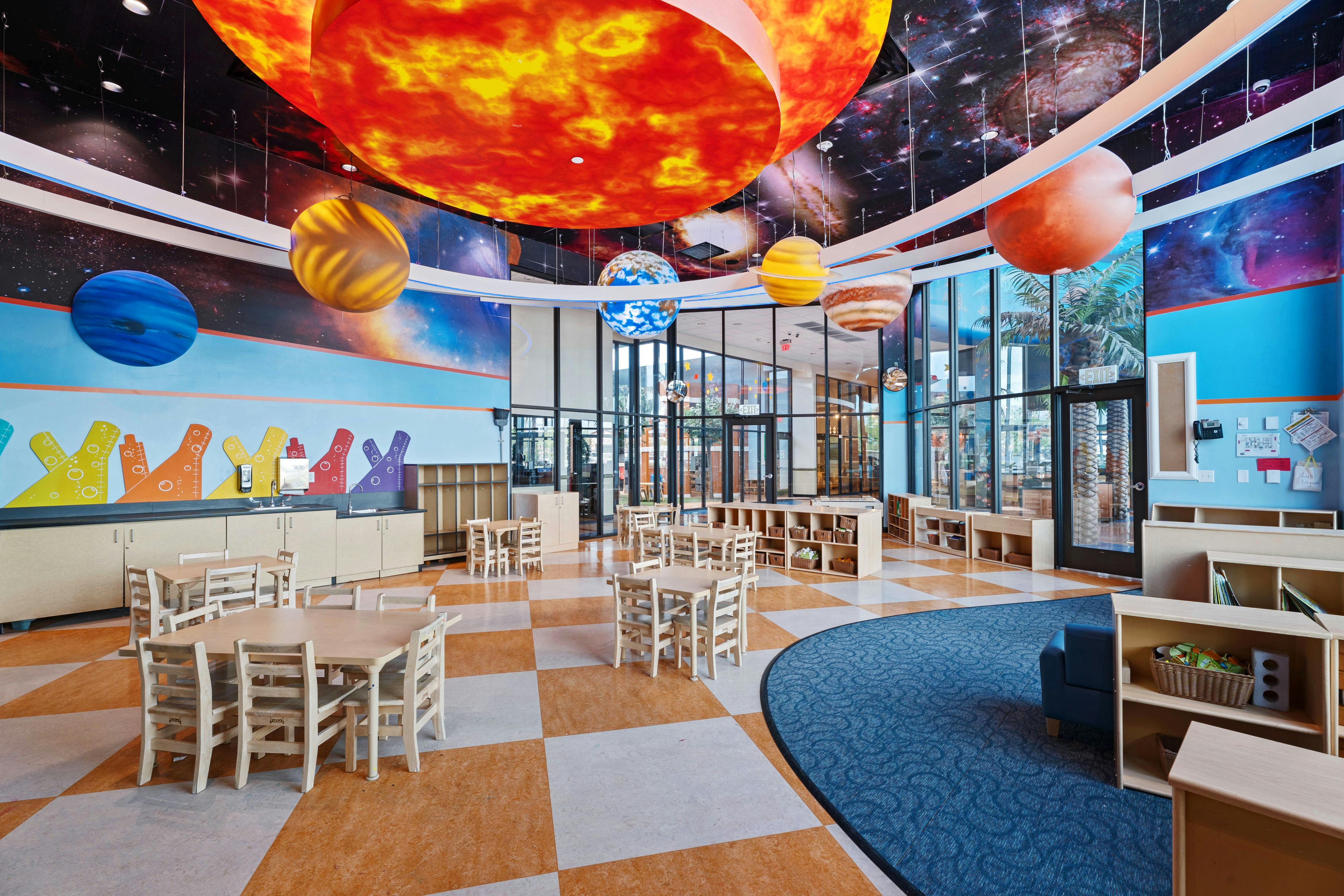 Classroom decorated with planets and solar system murals, small tables and chairs