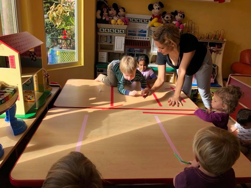 Adult and children drawing on a large table in a classroom