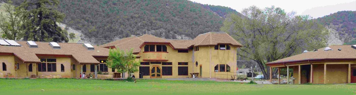 Large building with multiple sections and a brown roof, green lawn in front
