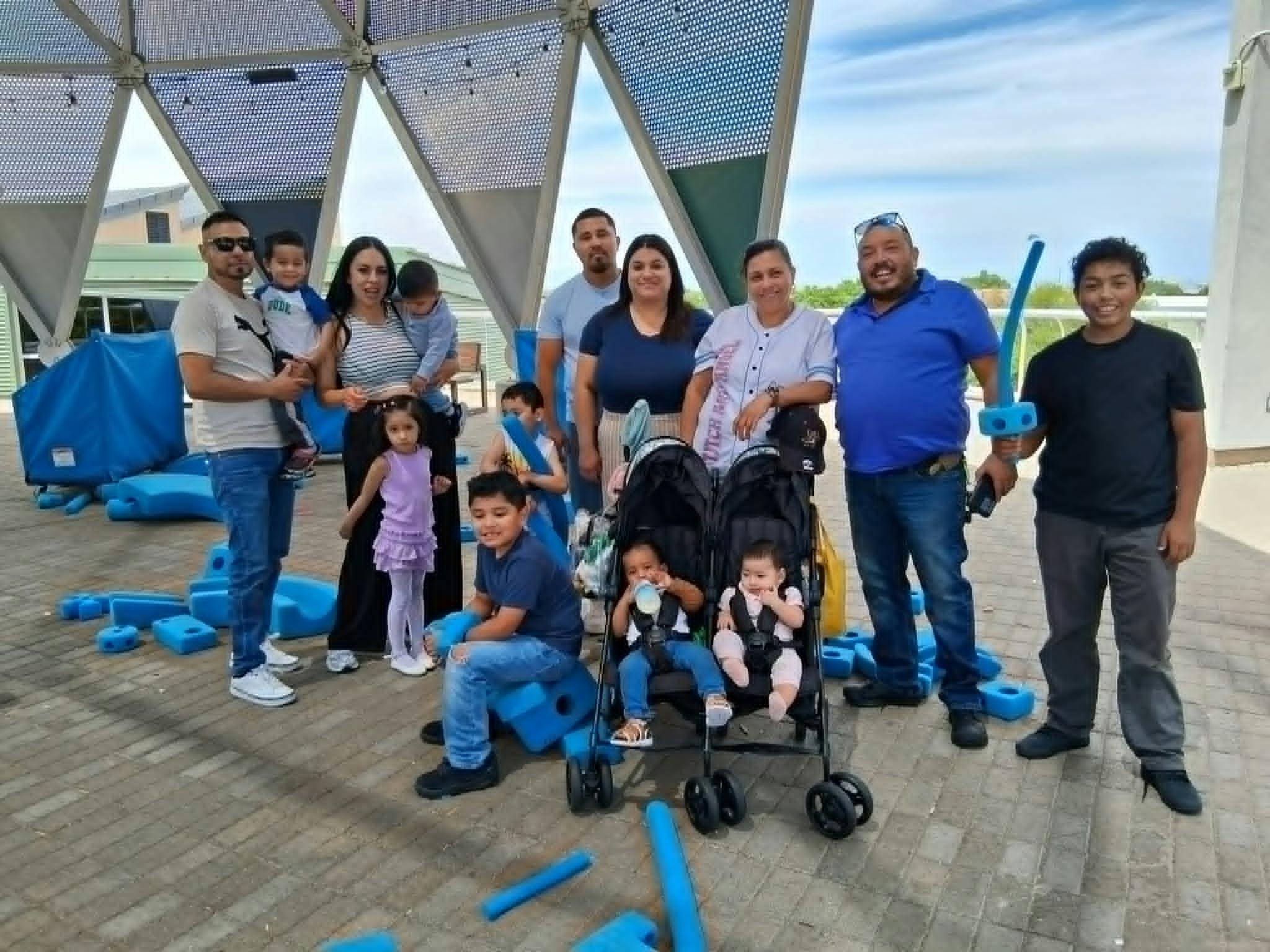 Group of adults and children posing outdoors with two babies in strollers