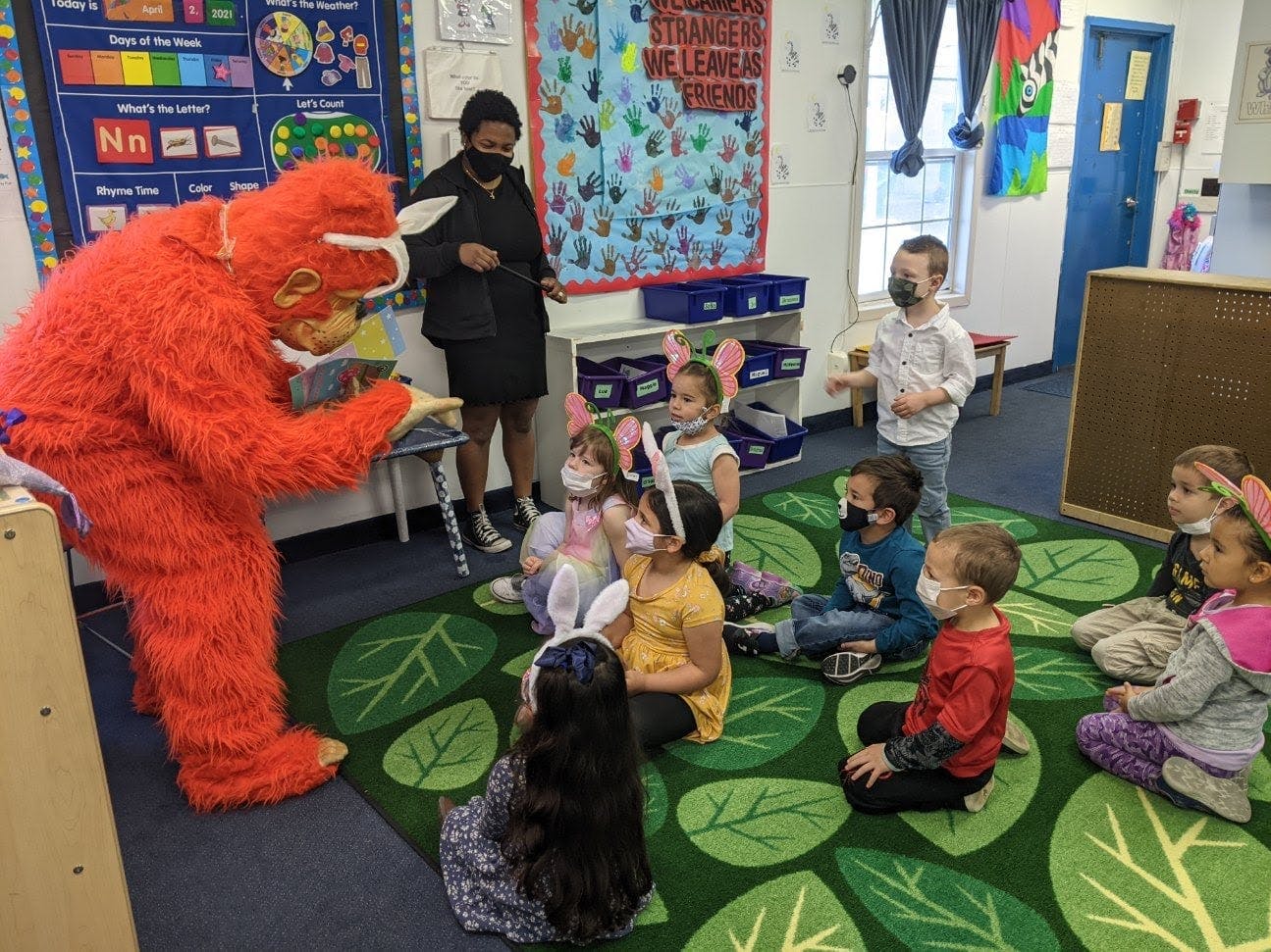 Person in red monster costume interacting with children in a classroom