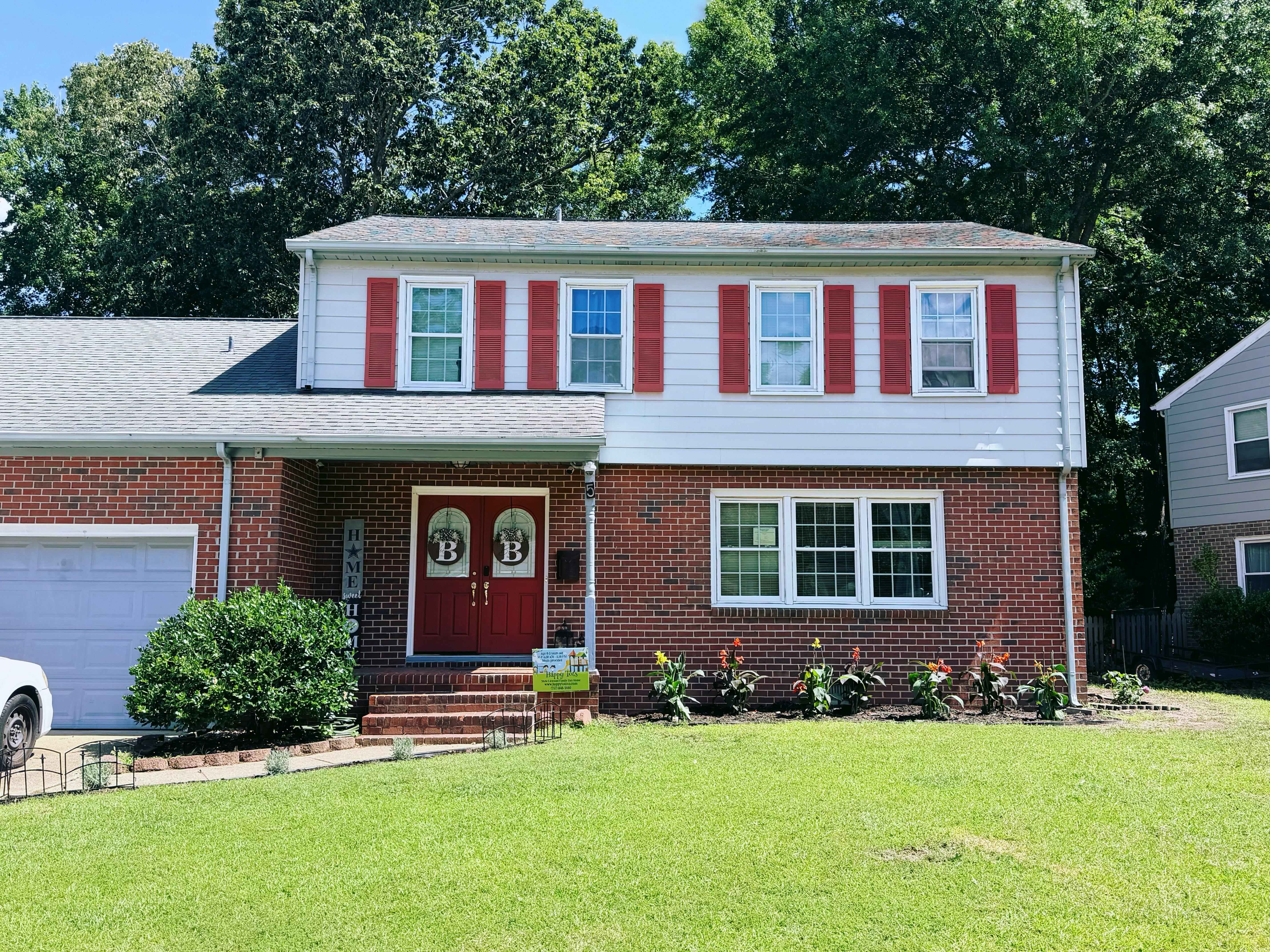 Two-story brick and white siding suburban house with red shutters