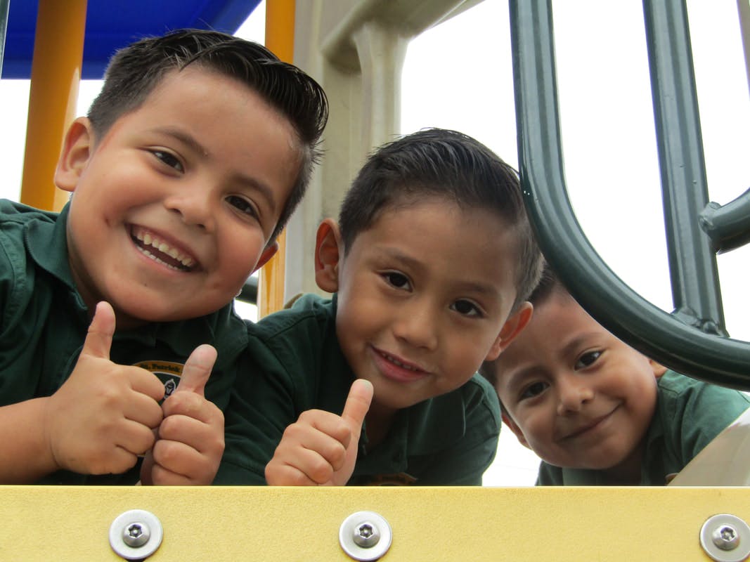 Three children on a playground, two giving thumbs up
