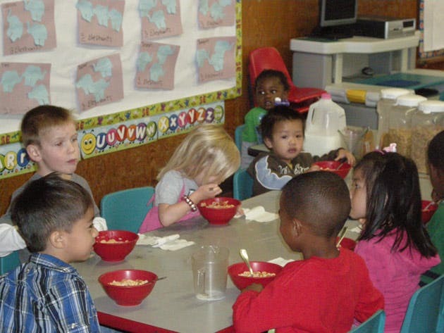 Children eating cereal at a table in a classroom