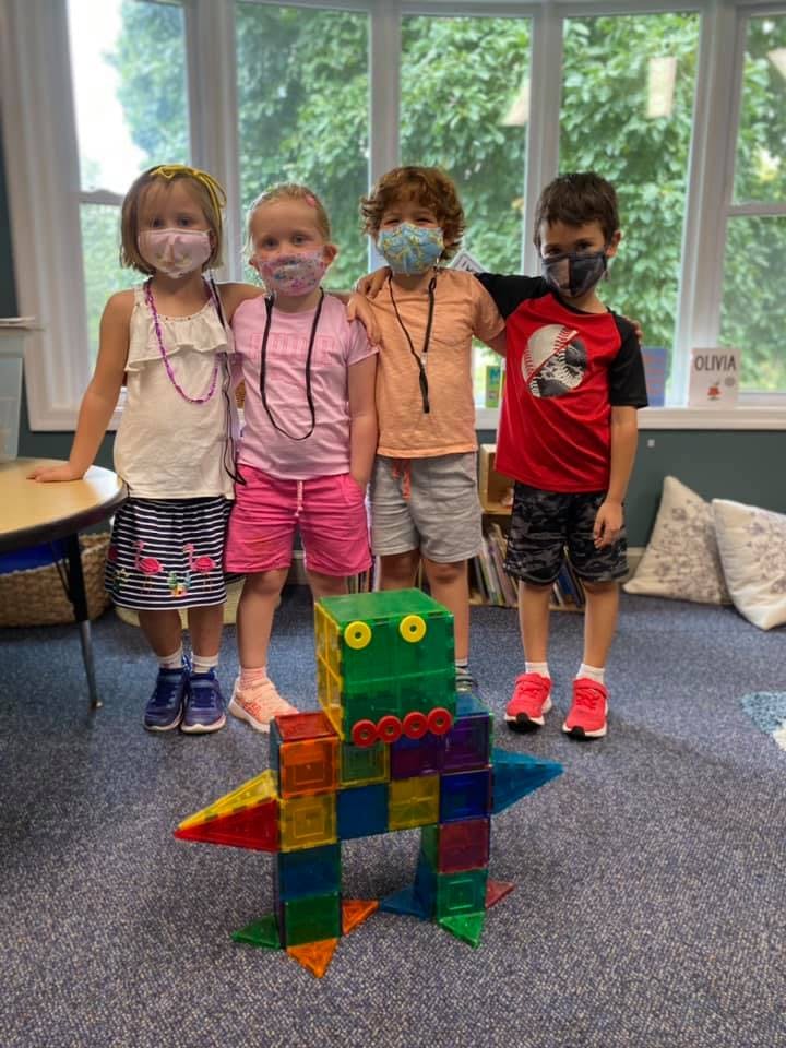 Four children wearing face masks standing behind a colorful block creation