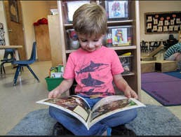 Child sitting on floor reading a book in a classroom