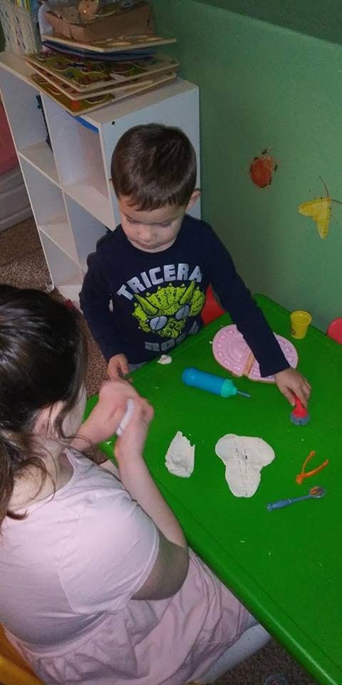 Child and person playing with modeling clay at a green table