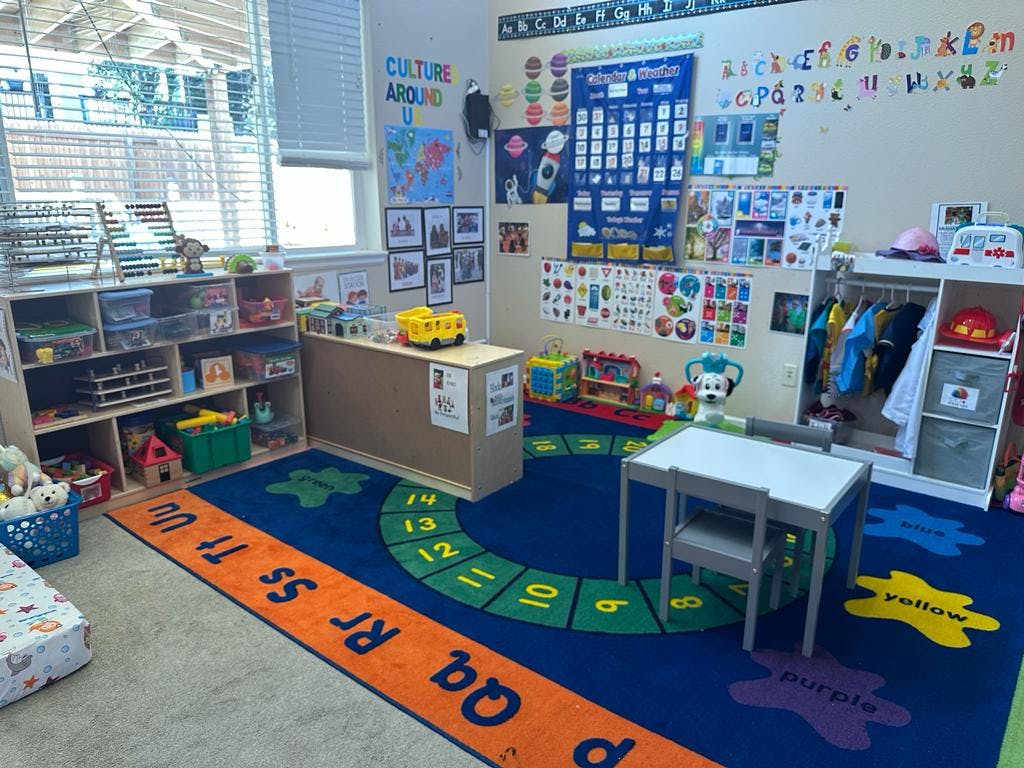 A colorful classroom with a blue rug, shelves, and a small table and chair