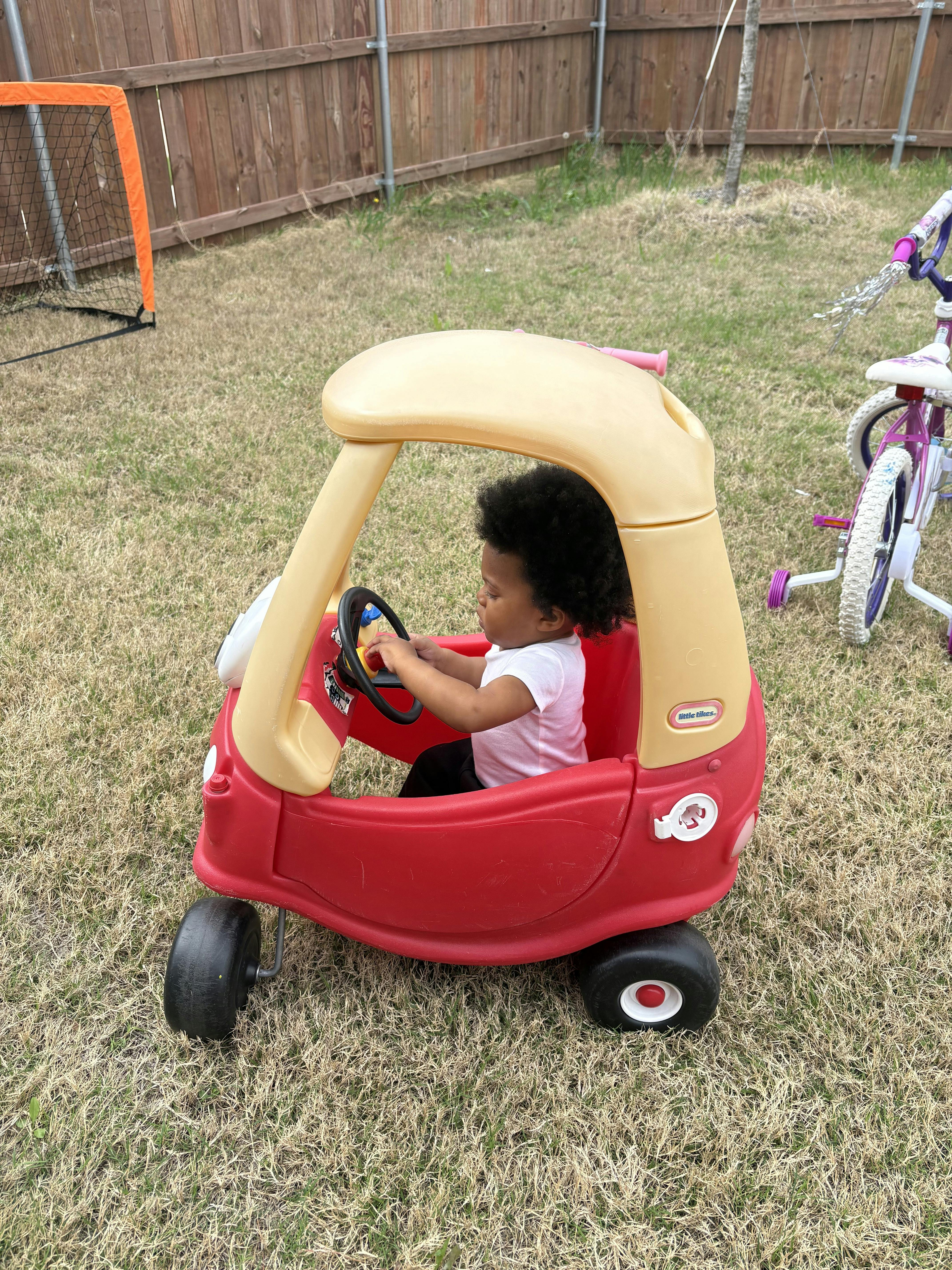 Child in a red and yellow toy car, grasping the steering wheel