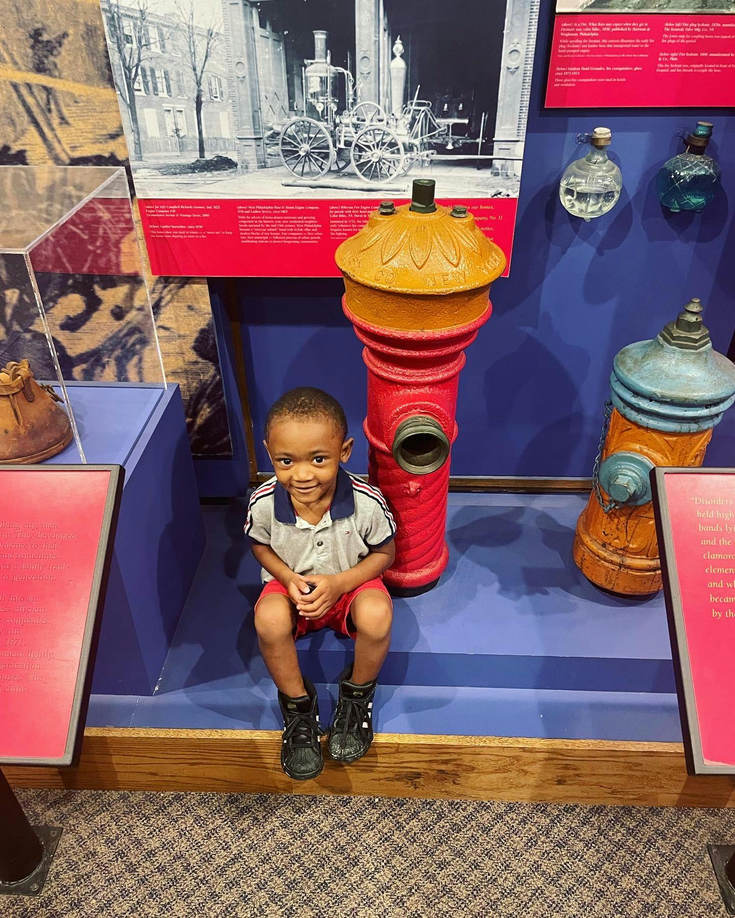 Child sitting next to a red fire hydrant display