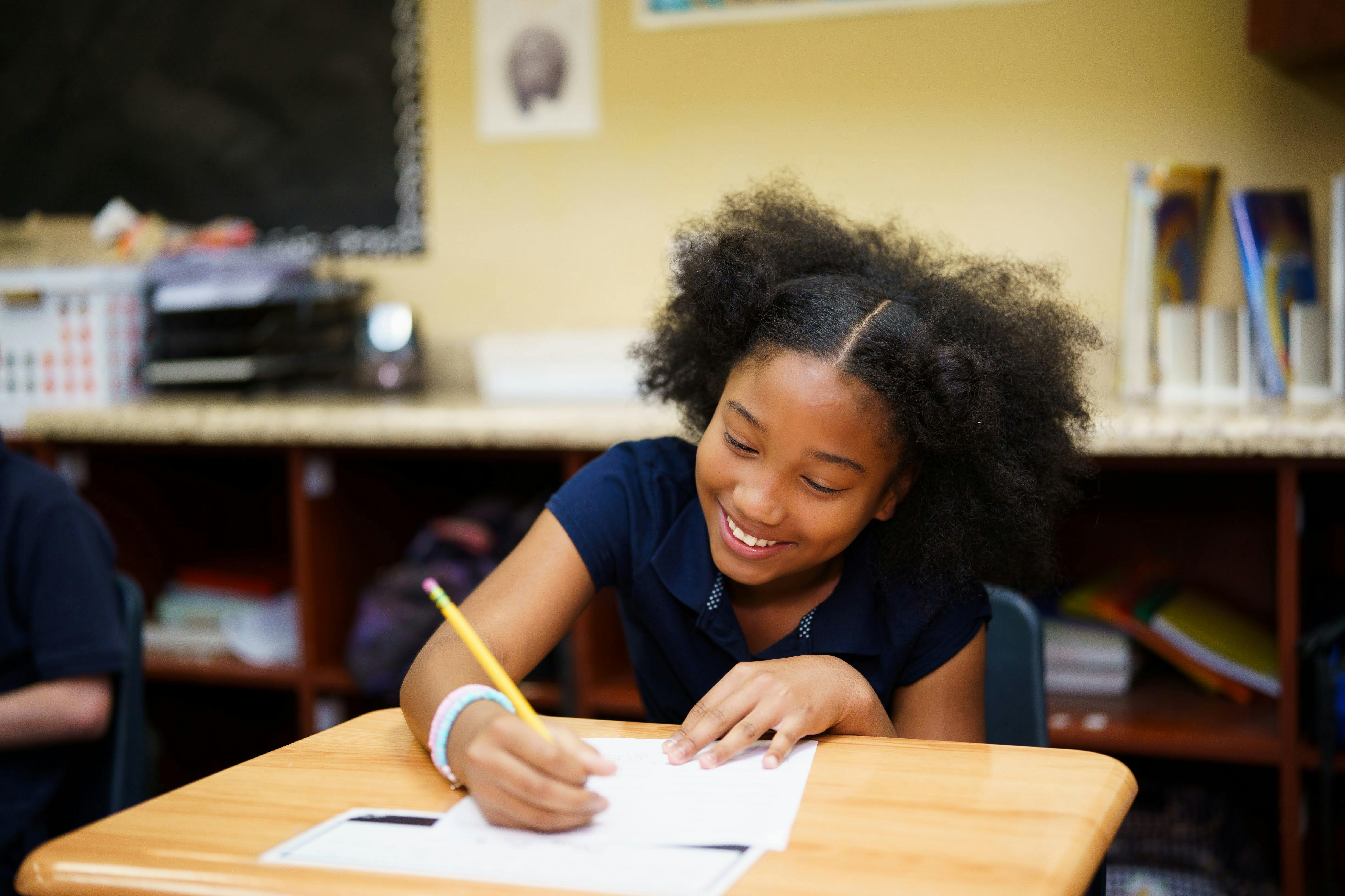 Child writing on paper at a desk in a classroom