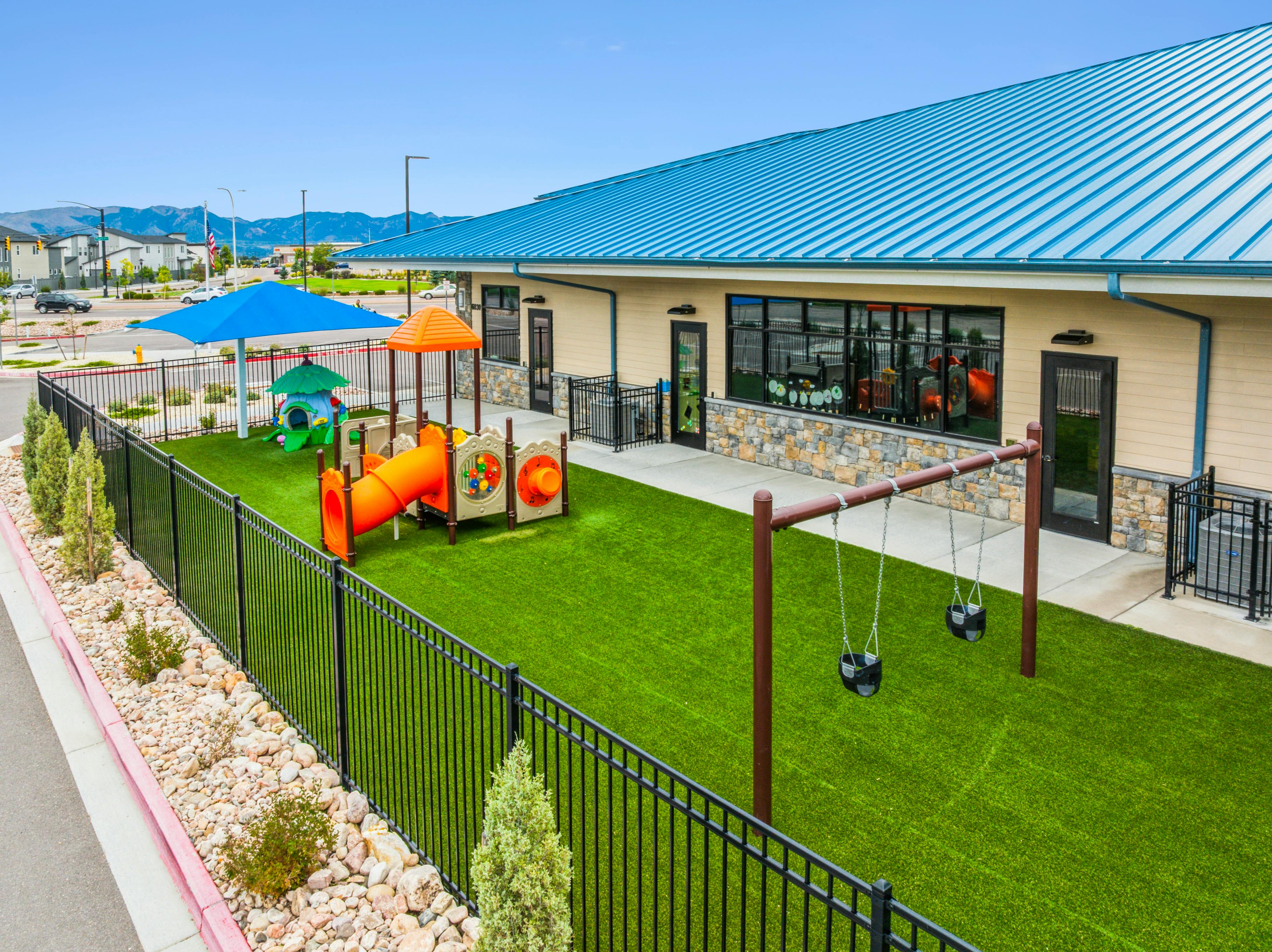 Playground with swings, orange slide, and small play structures next to a building