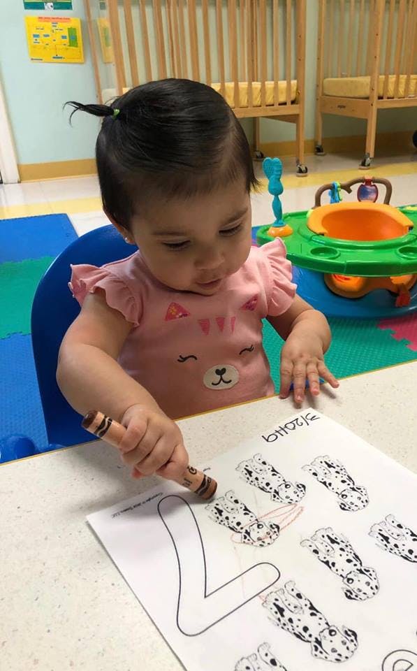 Child coloring a letter on a paper with a crayon