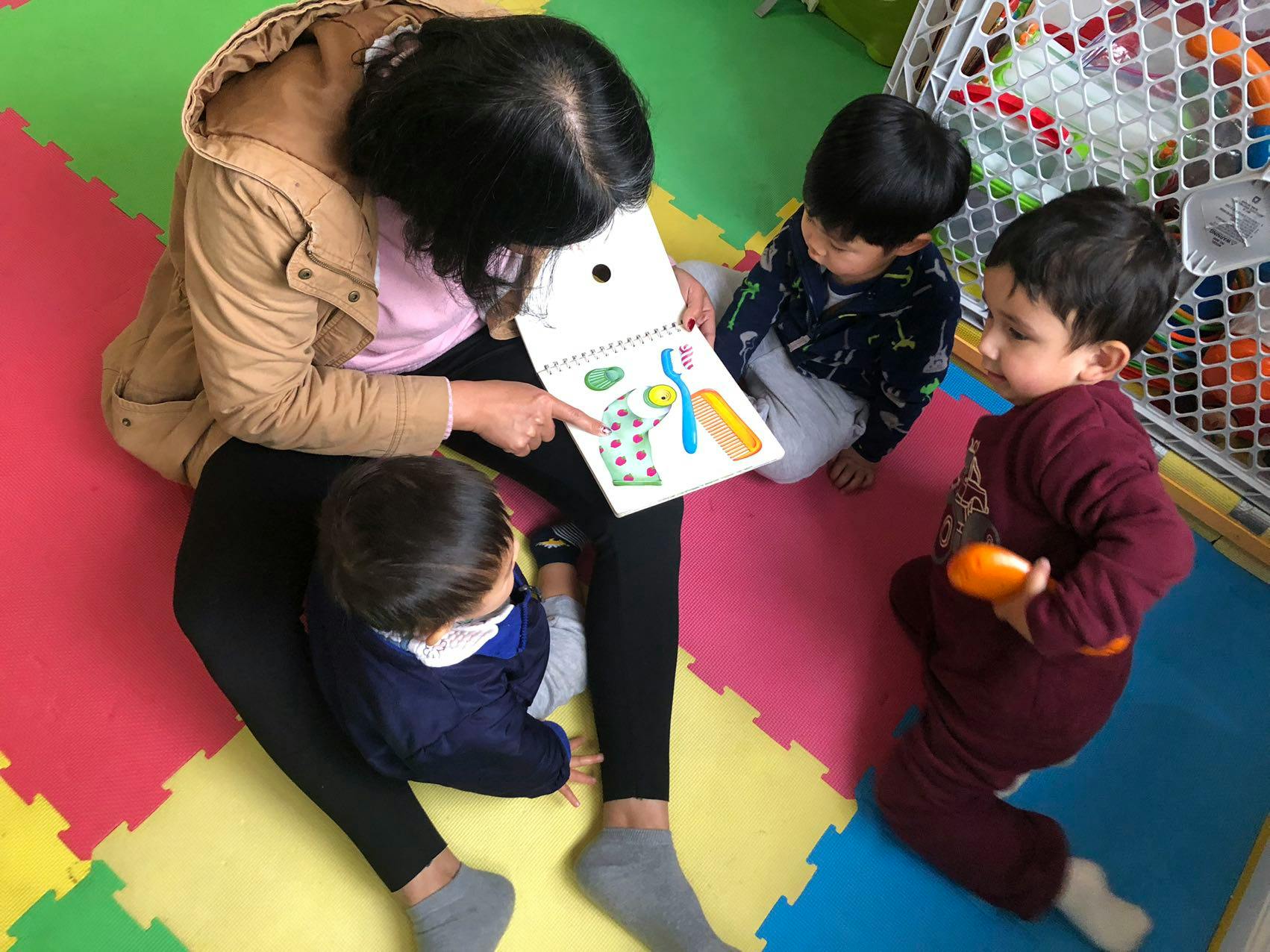 Person reading a book to three children on a colorful mat
