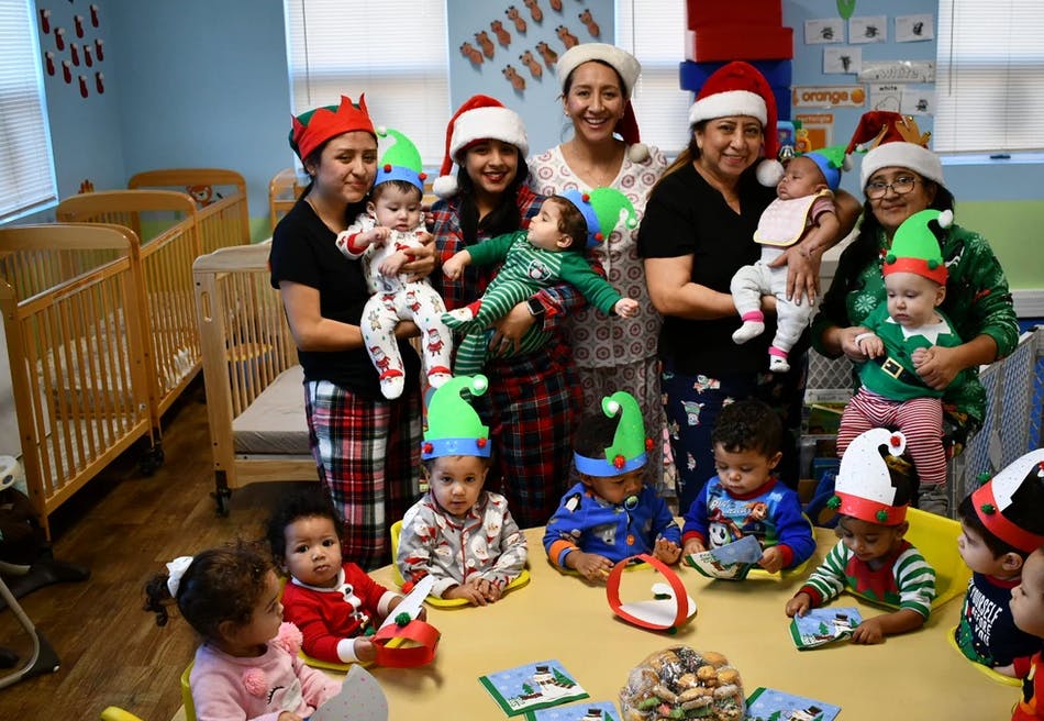 Adults and children in holiday hats in a room with cribs